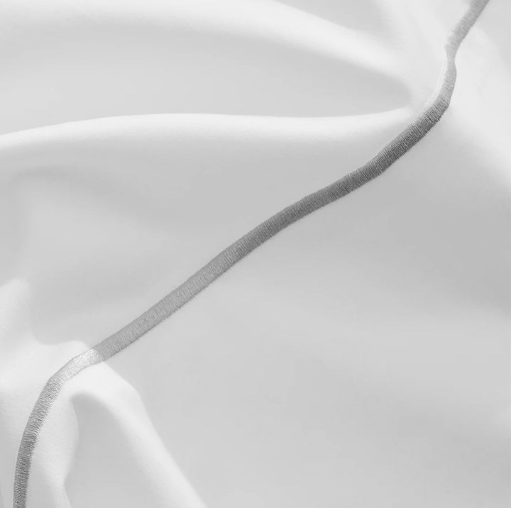 Close-up of white organic cotton fabric with single-line embroidery, showcasing luxe sateen weave and fine detailing.